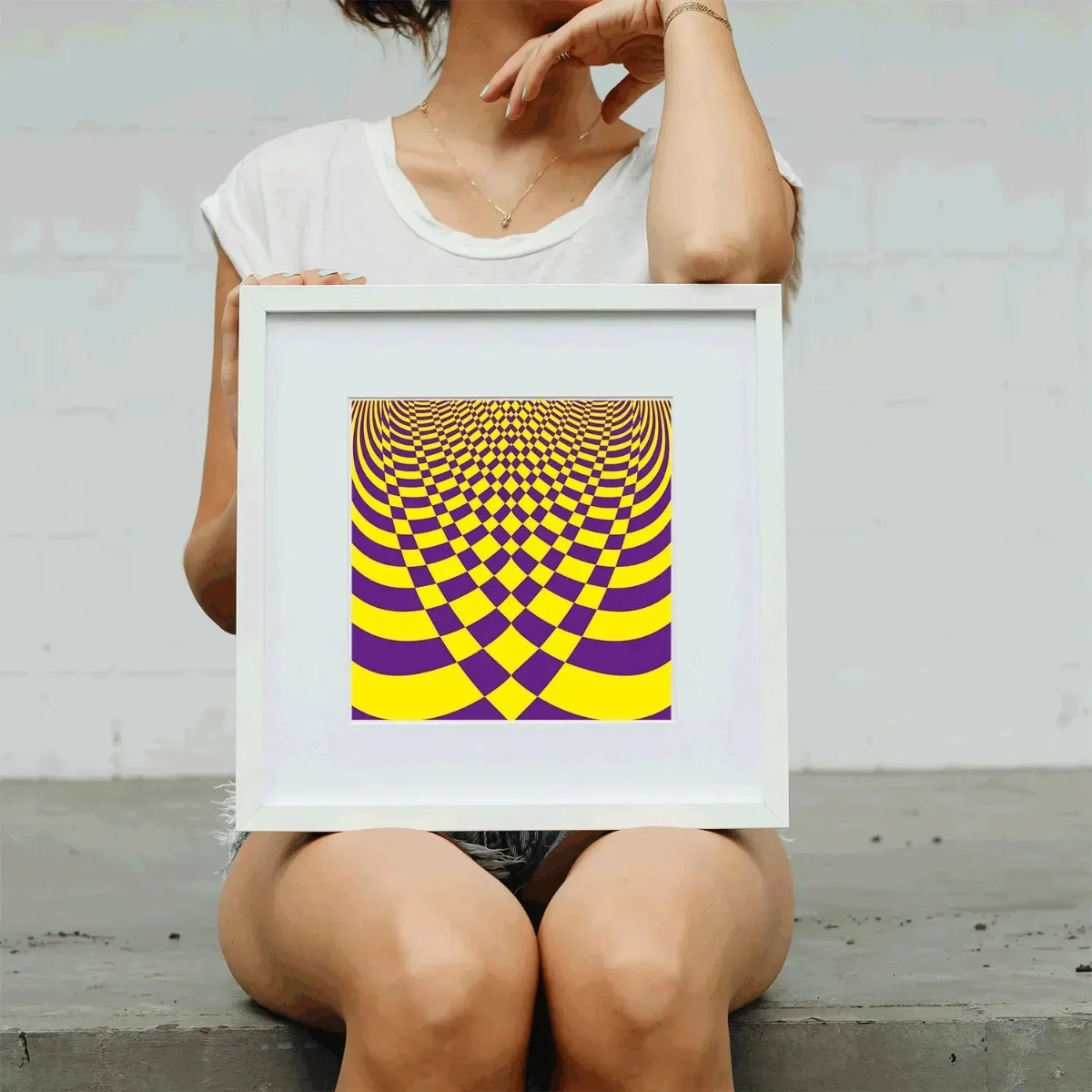Person holding a framed yellow and purple checkered optical illusion poster.