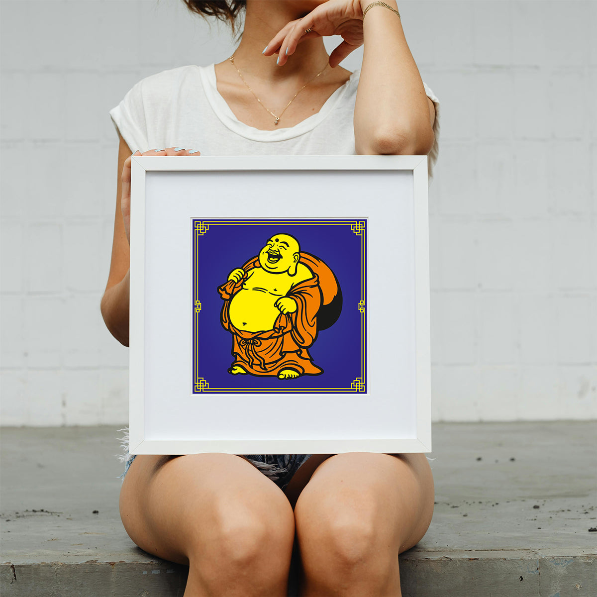 Person holding a framed artwork of a laughing Buddha on a plain background