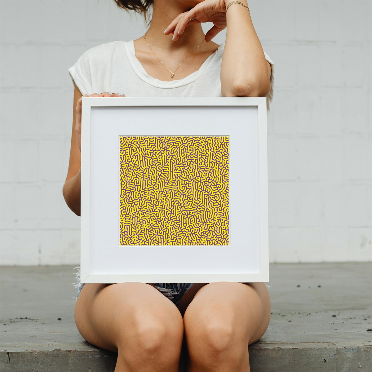 Person holding a framed artwork with a yellow pattern against a plain background