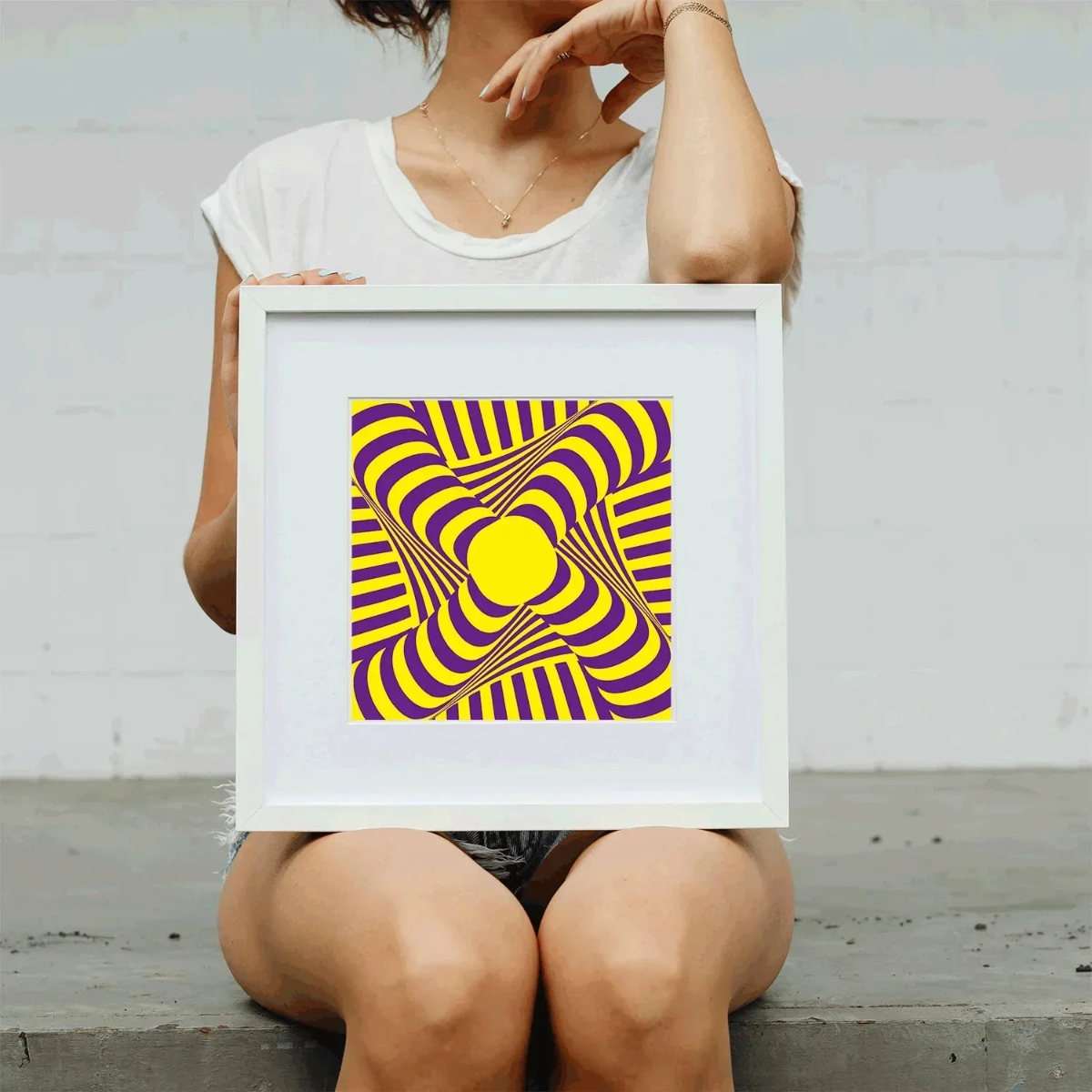 Person holding a framed abstract art print with yellow and purple design.