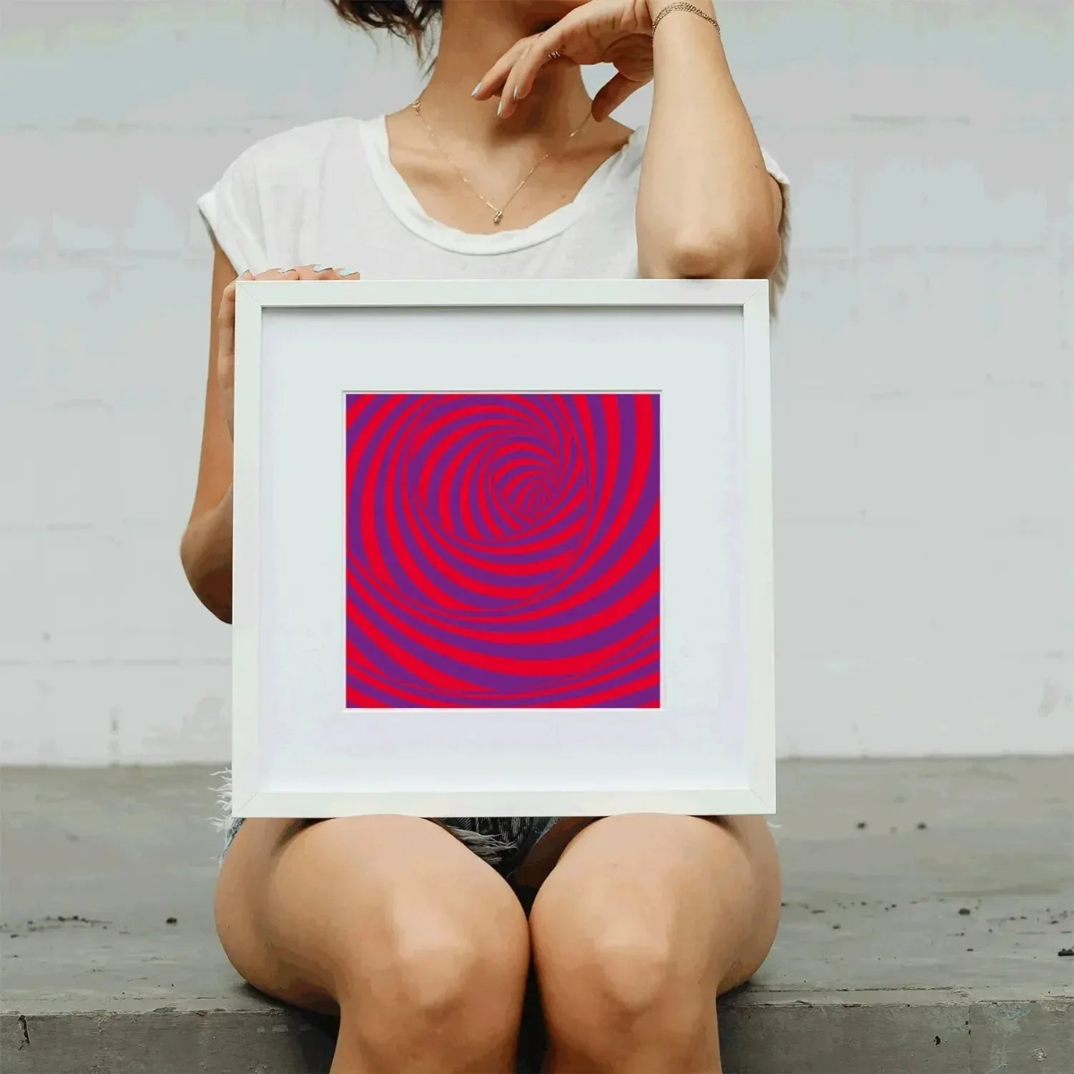 Person holding a framed artwork with a red and purple spiral pattern against a light gray background.