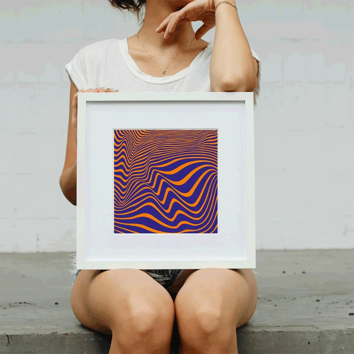Person holding a framed abstract artwork with wavy lines in orange and purple against a light gray background.