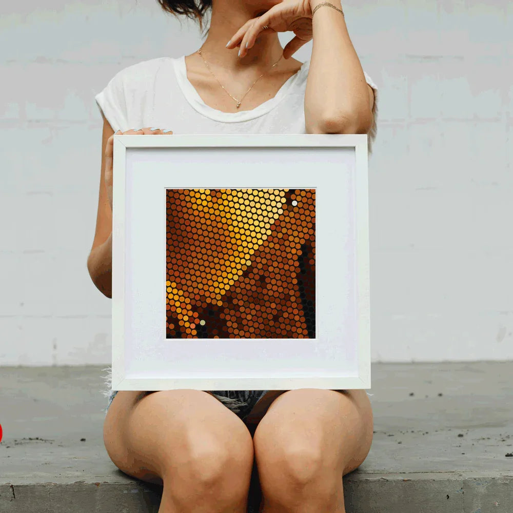 Person holding a framed artwork with a geometric pattern against a plain background