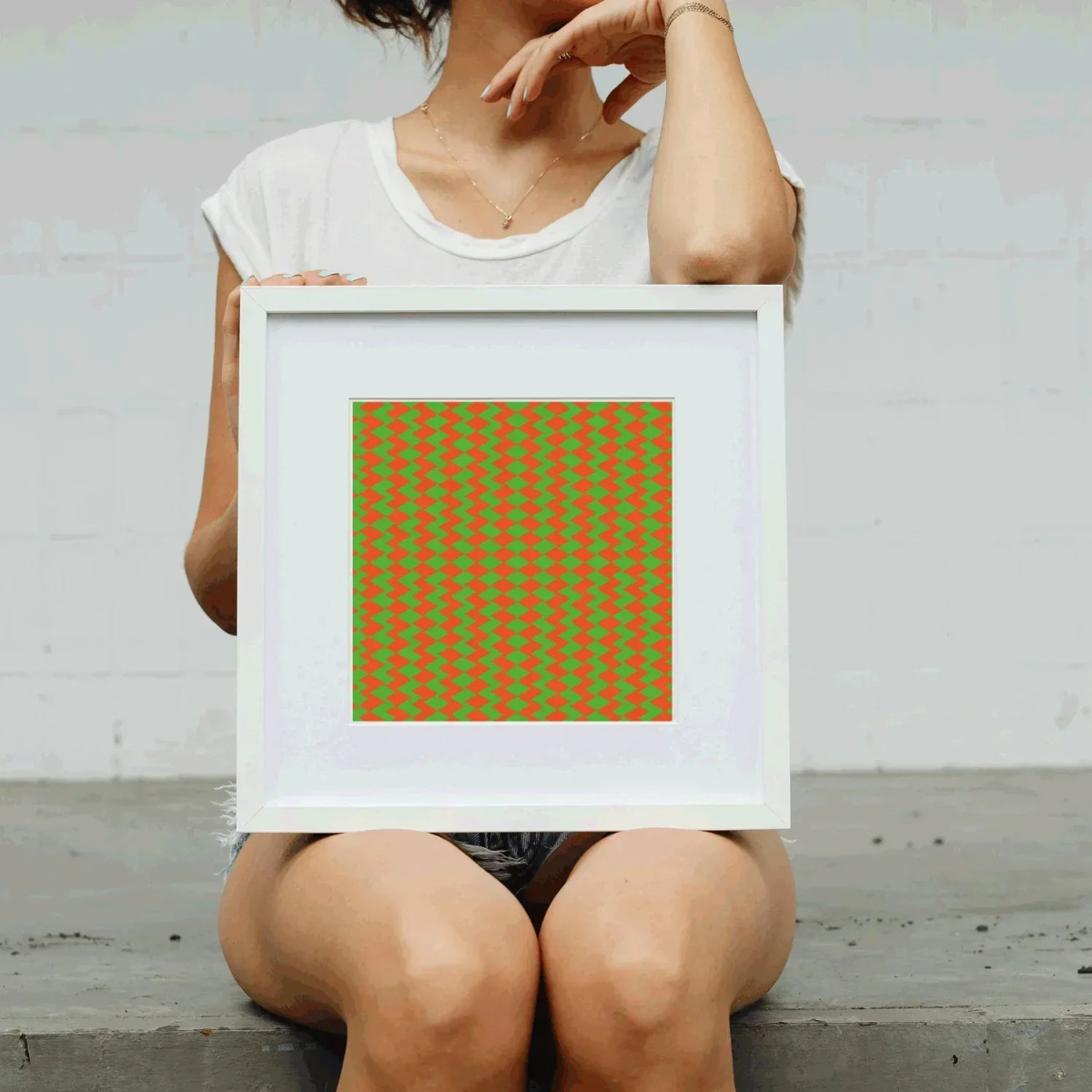 Person holding a framed artwork with a geometric pattern on a plain background