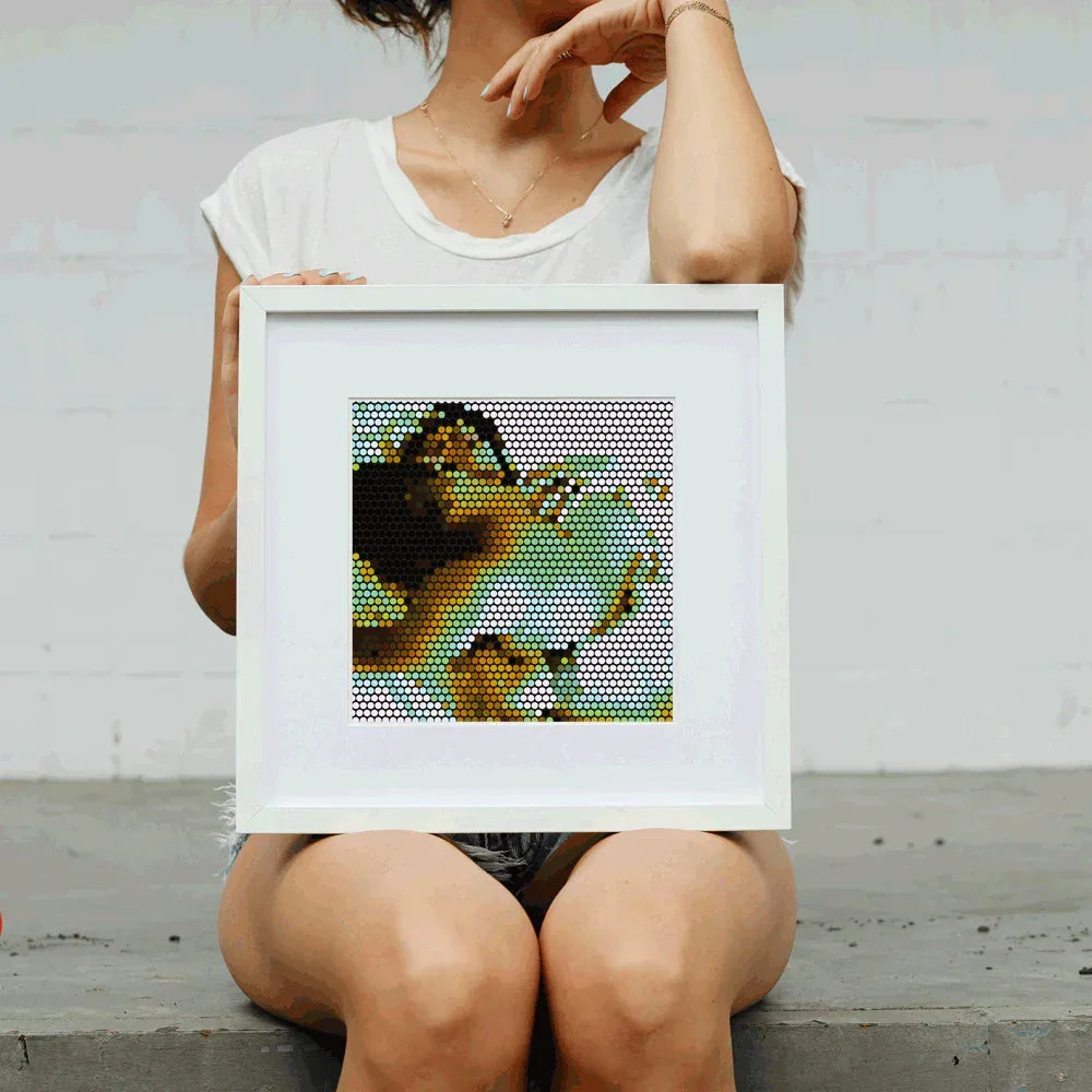 Person holding a framed mosaic artwork of a woman against a plain background