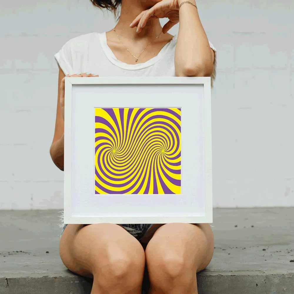 Person holding a framed yellow and purple spiral art print against a plain background