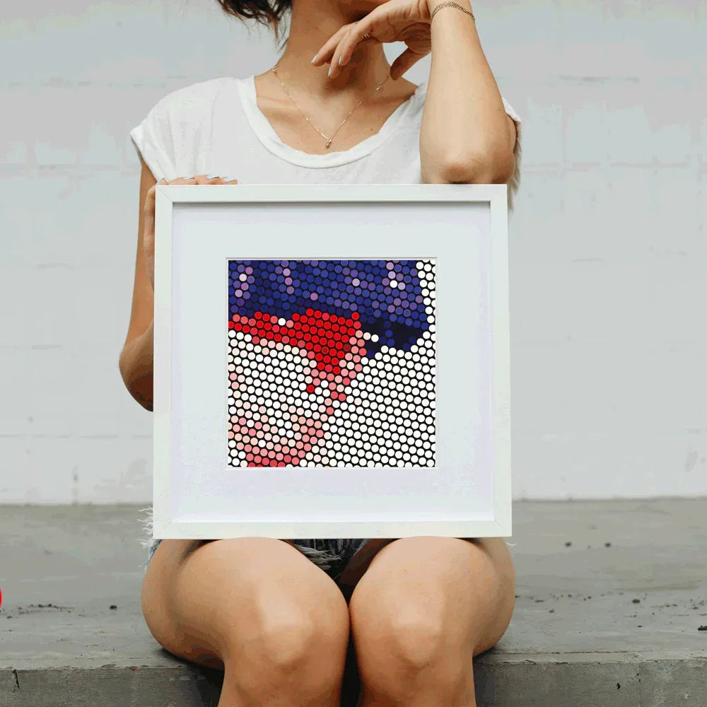 Person holding a framed artwork with a geometric design on a plain background