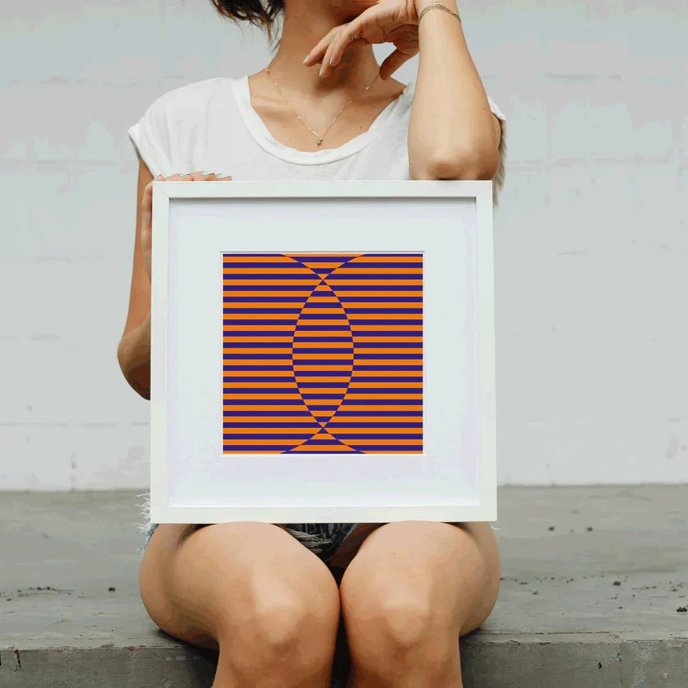Person holding a framed abstract artwork with orange and blue stripes against a light gray background