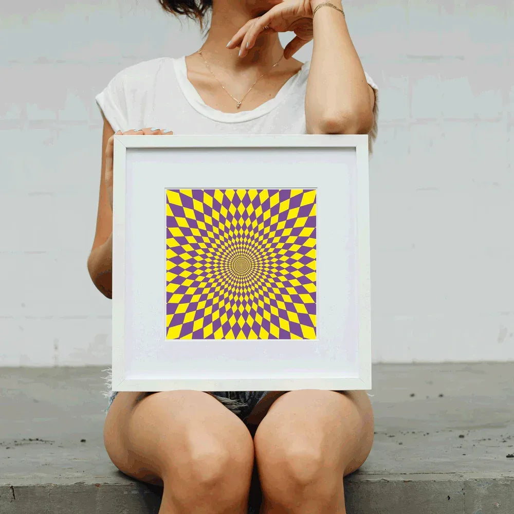 Person holding a framed purple and yellow optical illusion art print.