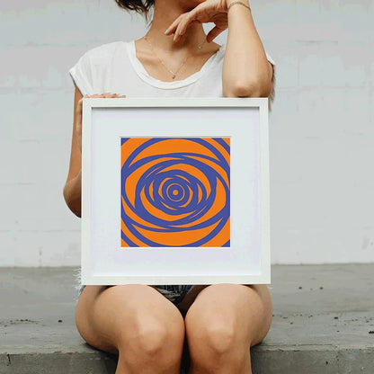 Person holding a framed orange and blue spiral art print against a plain background