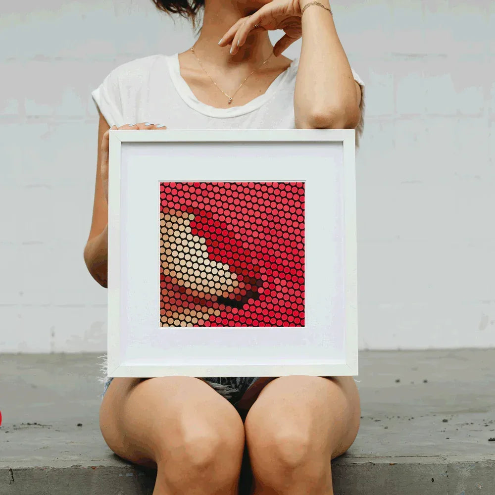 Person holding a framed artwork with a geometric pattern.