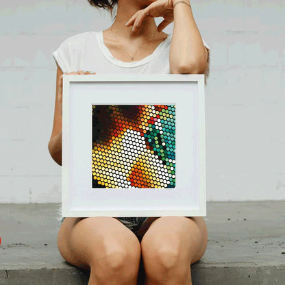 Person holding a framed colorful abstract art piece against a plain background
