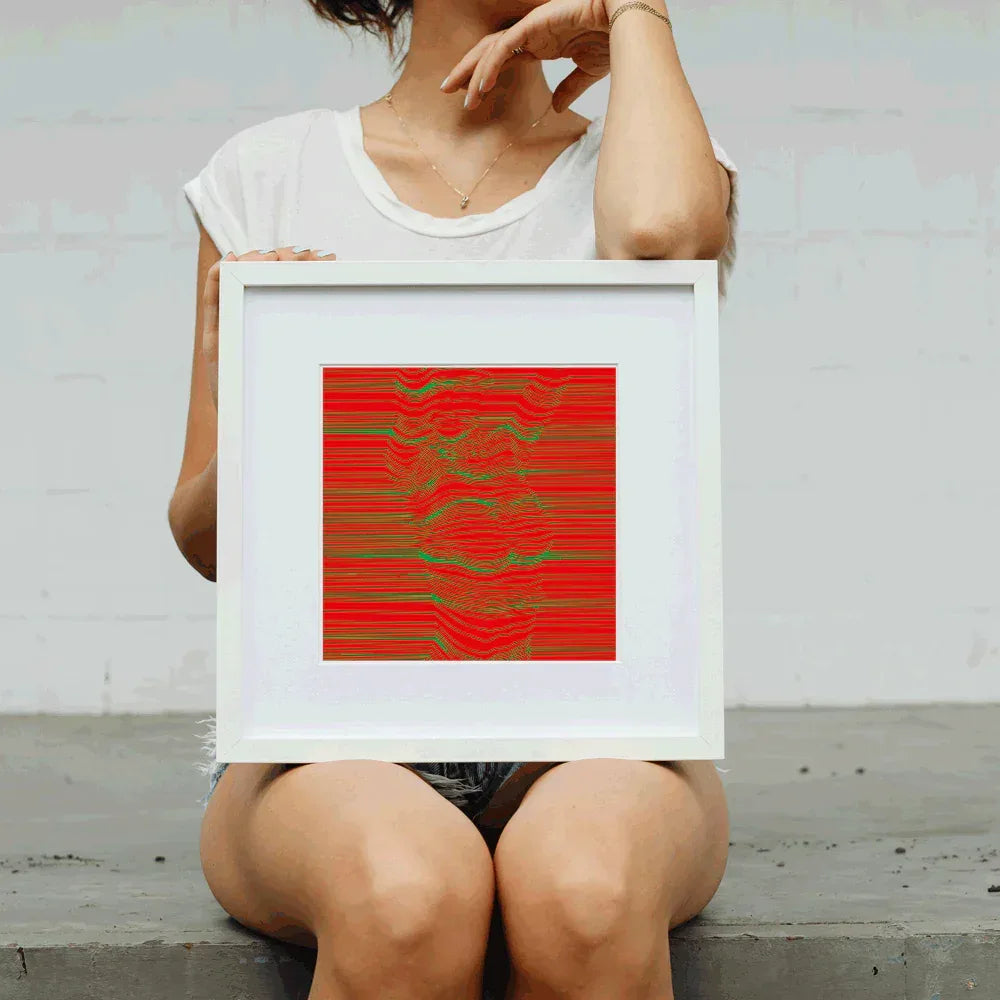 Person holding a framed abstract artwork with red and green patterns.