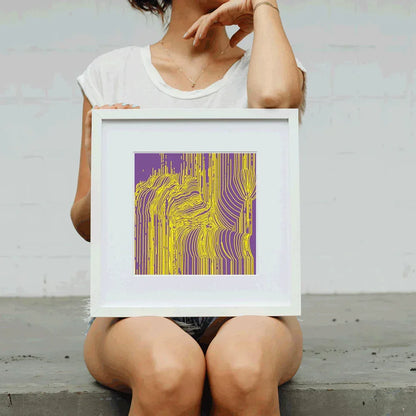 Person holding a framed abstract art print with purple and yellow design.